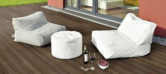 Terrasse mit dunklen Thermo-Esche-Dielen, bequemen Sitzsäcken, weißem Pouf und stilvoll arrangiertem Wein und Snacks.